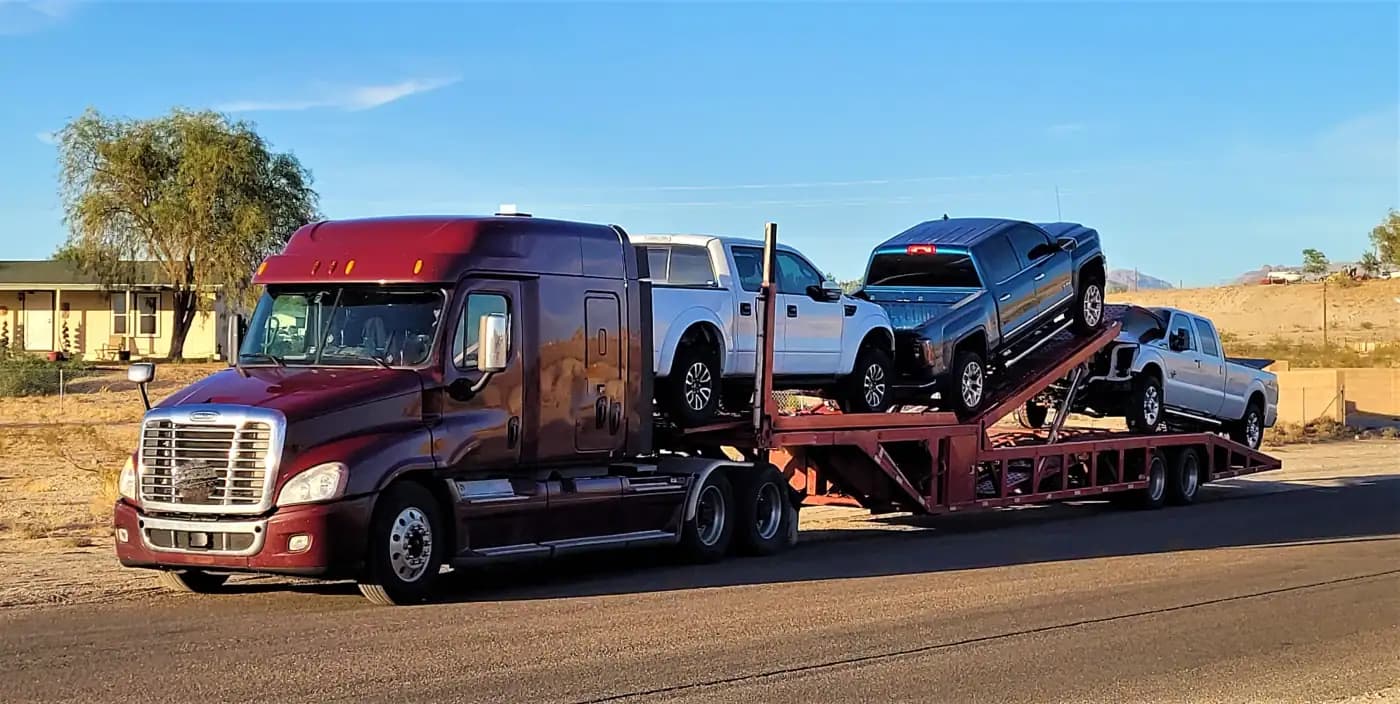 Open car carrier transporting pickup trucks