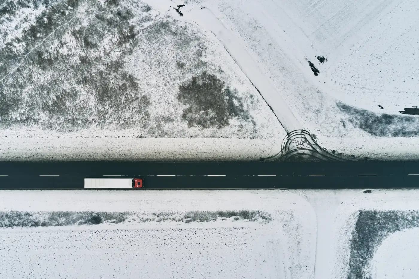 Aerial view of a truck on a road through snowy fields