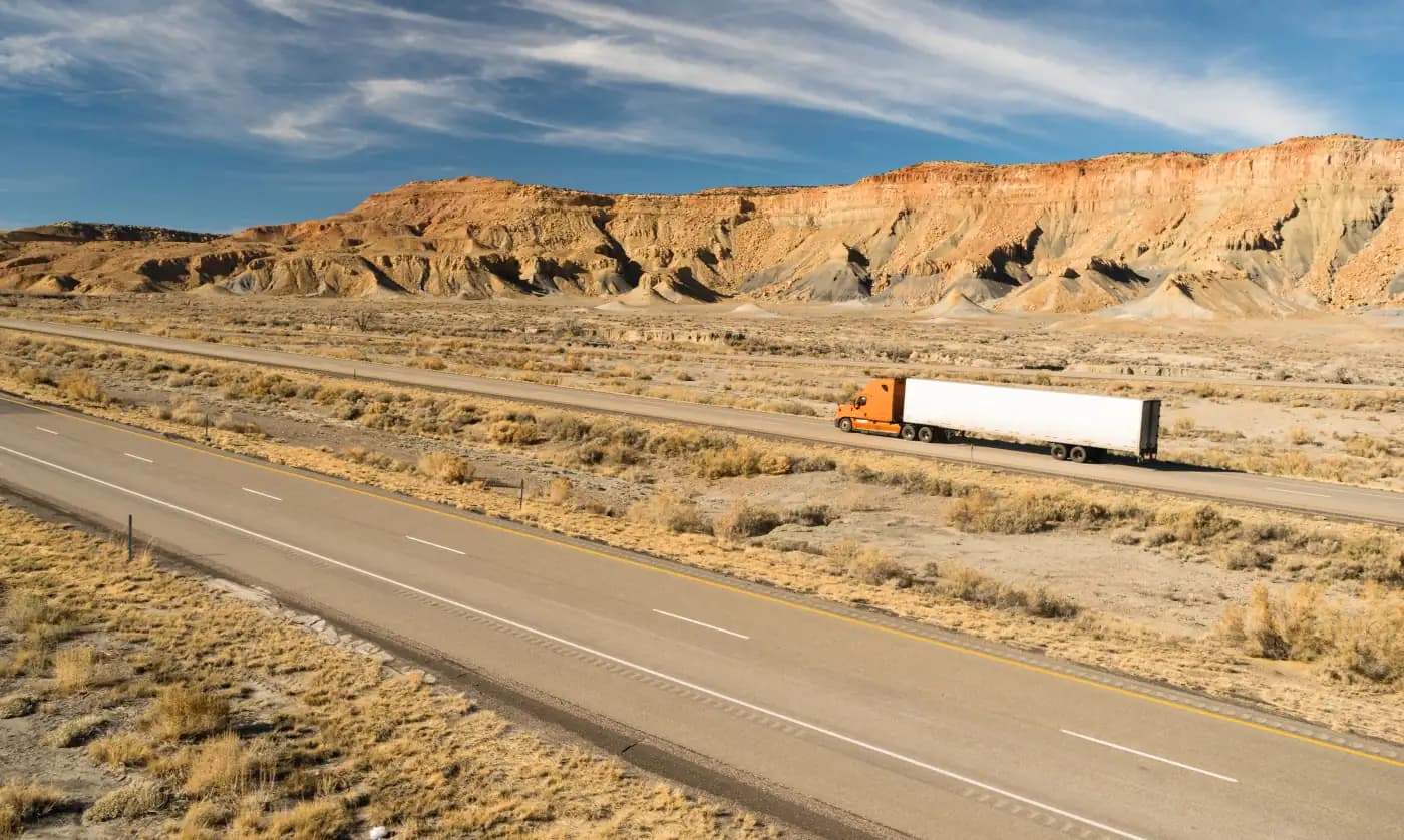 Tractor-trailer traveling beneath desert cliffs
