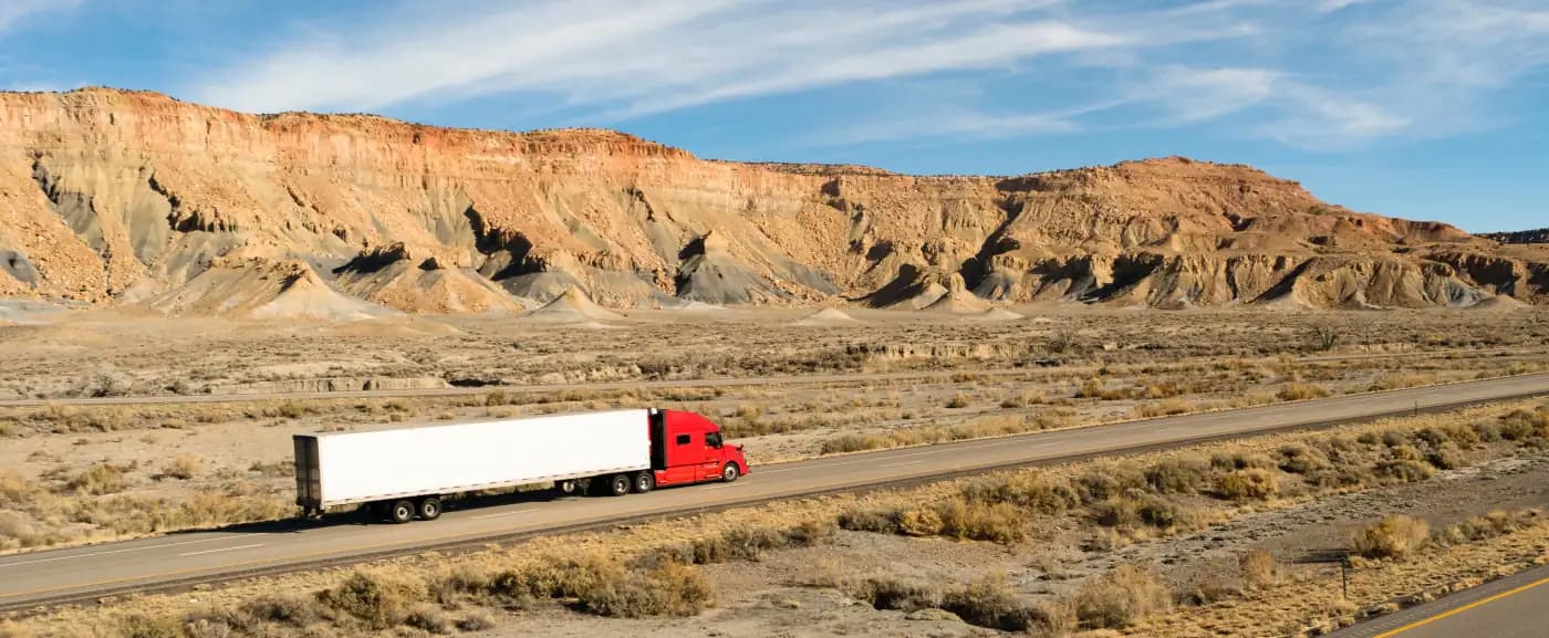 Red tractor-trailer beneath desert cliffs