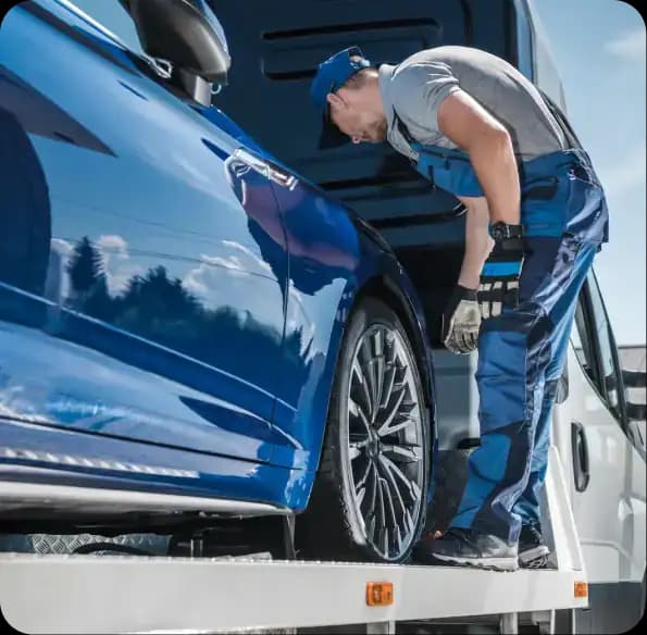 Worker securing a blue car on a recovery truck