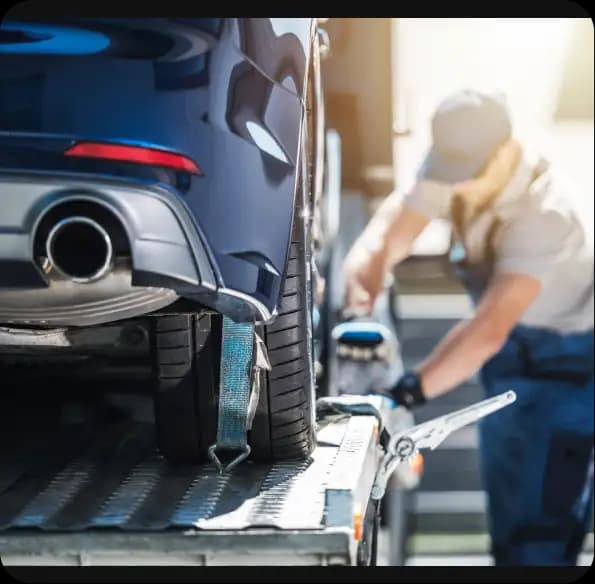Worker securing a blue car on a recovery truck