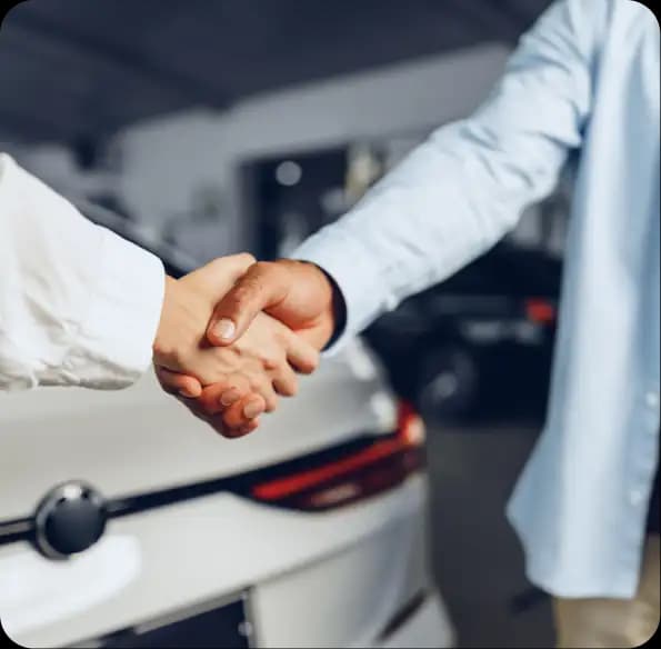 Two people shaking hands beside a car