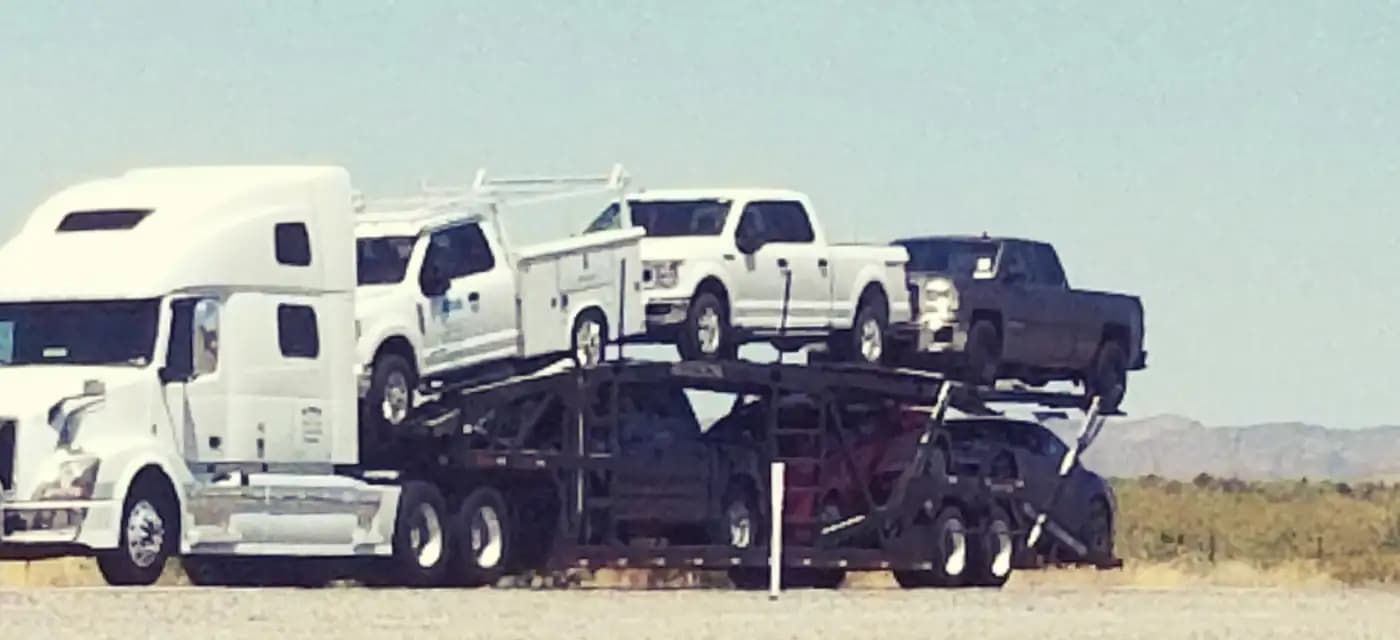 Open car carrier transporting pickup trucks