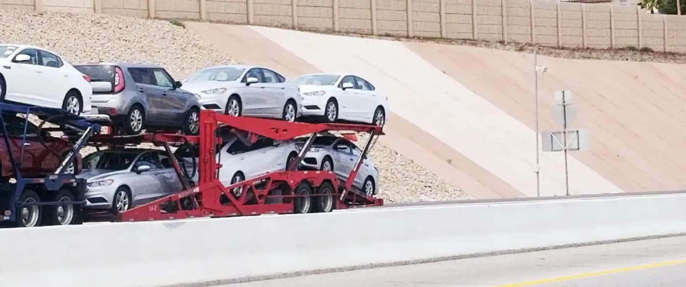 Open car carrier loaded with cars beside a highway barrier