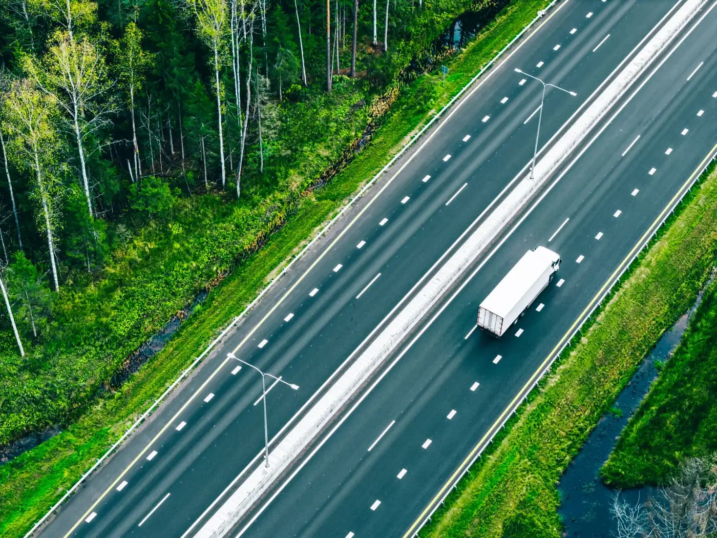Aerial view of a truck on a highway through green woodland