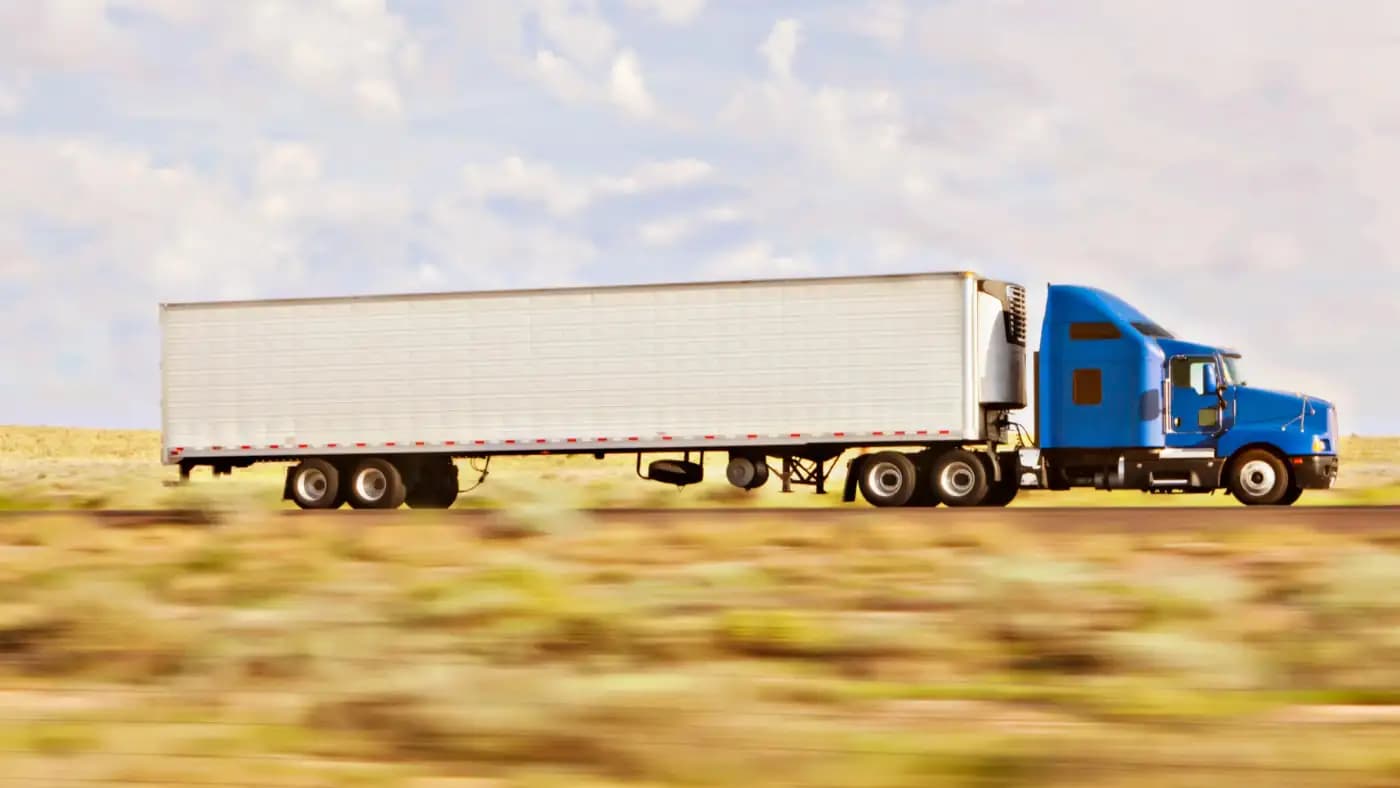 Blue semi-truck hauling a white trailer through grassland