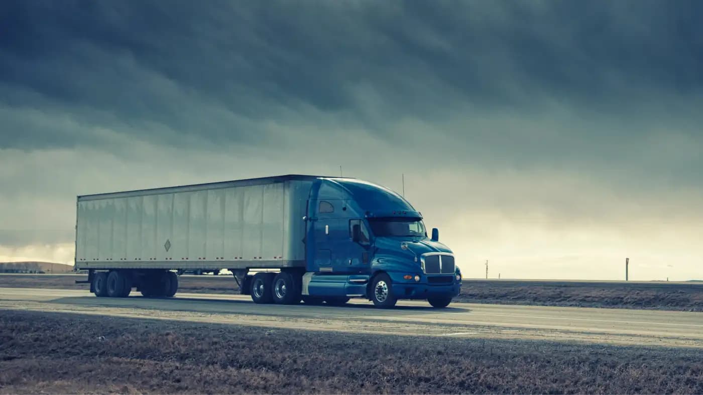 Blue tractor-trailer beneath dark clouds