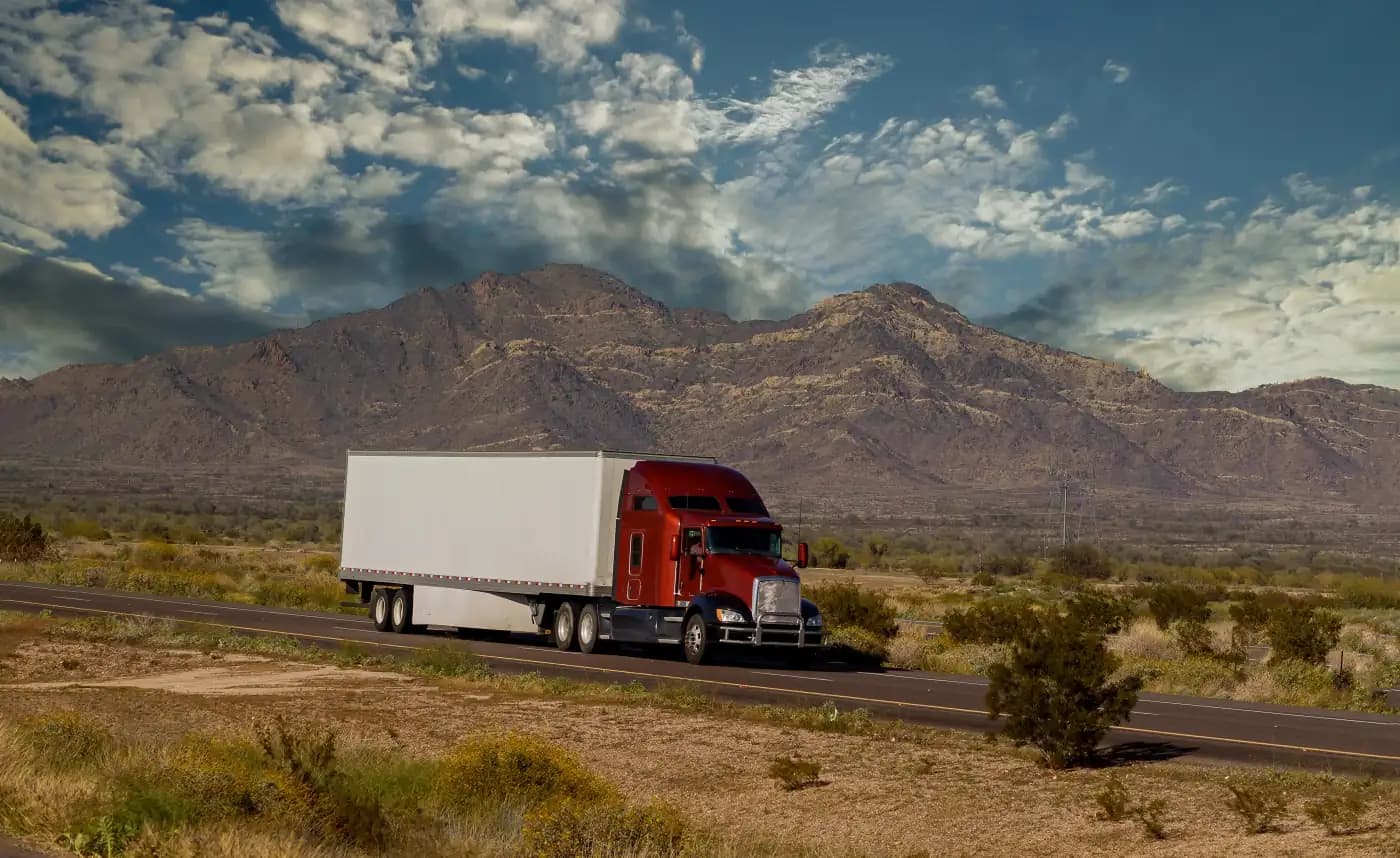 Red semi-truck with a white trailer beside desert mountains
